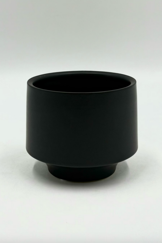 The Soft Spoken planter in matte black with rounded shape and subtle footed base on a neutral backdrop.