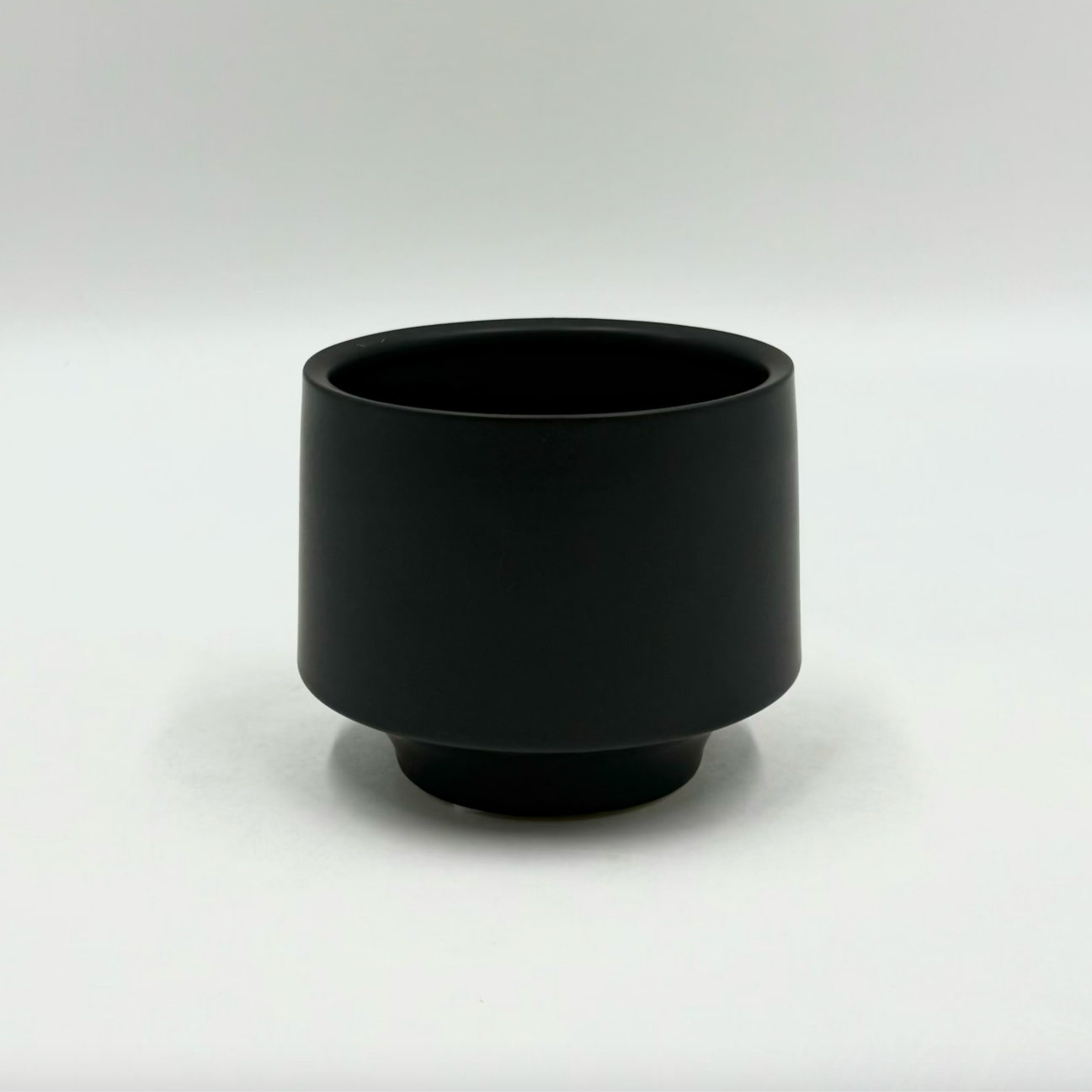 The Soft Spoken planter in matte black with rounded shape and subtle footed base on a neutral backdrop.