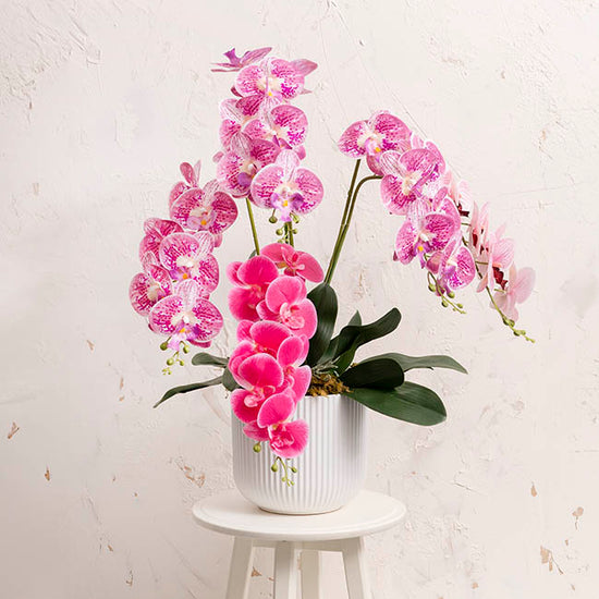 The Effortless Fit white matte planter holding vibrant pink orchids, styled on a small white table.