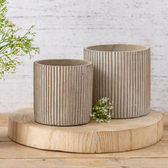Two ceramic pots with striped design on a wooden stand against a light brick wall.