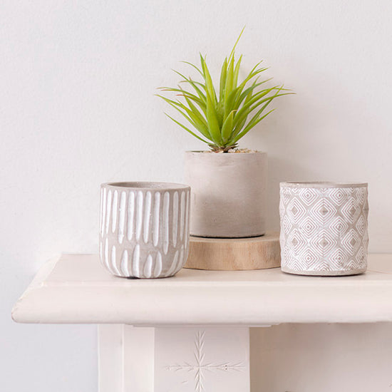 The Quiet Achiever cement planter styled with other neutral pots and greenery on a white shelf in soft natural lighting.