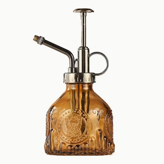 Vintage brown glass plant mister with pump nozzle on a neutral background.